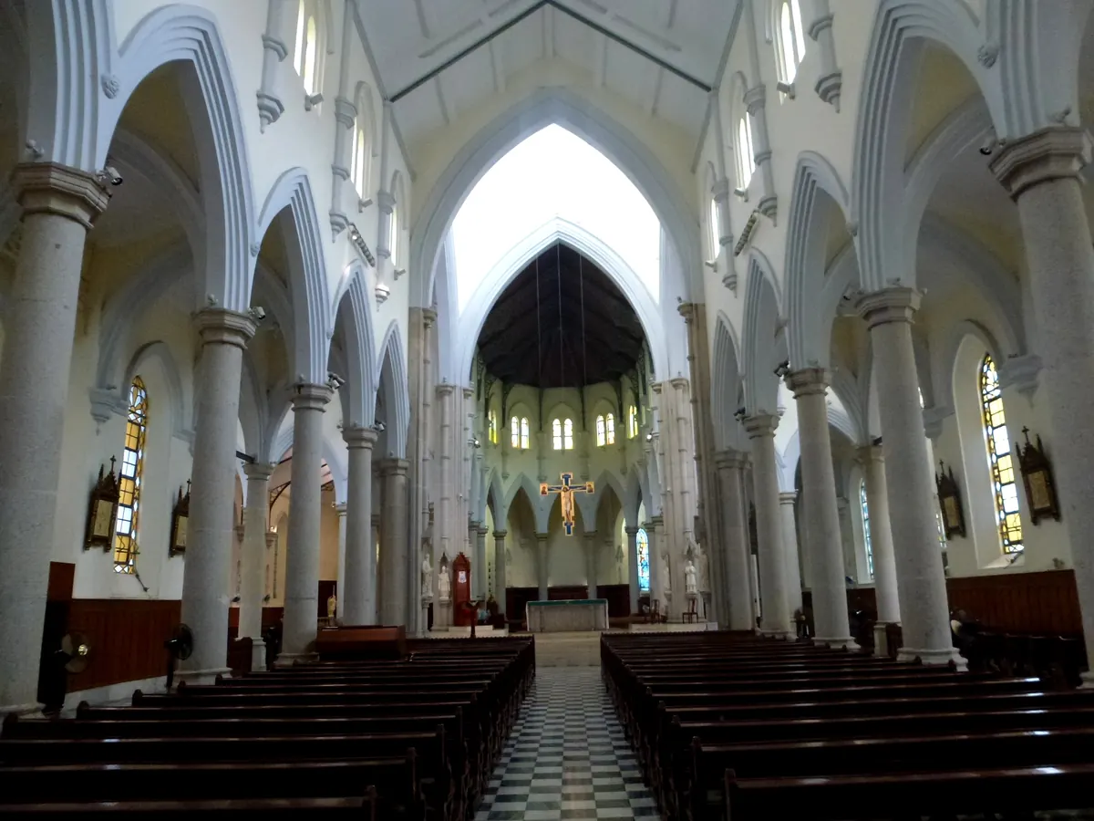 The long nave of the Cathedral of the Immaculate Conception on Caine Road: white Gothic arches, granite columns, dark wooden pews and a chequered aisle leading to a golden crucifix above the altar.