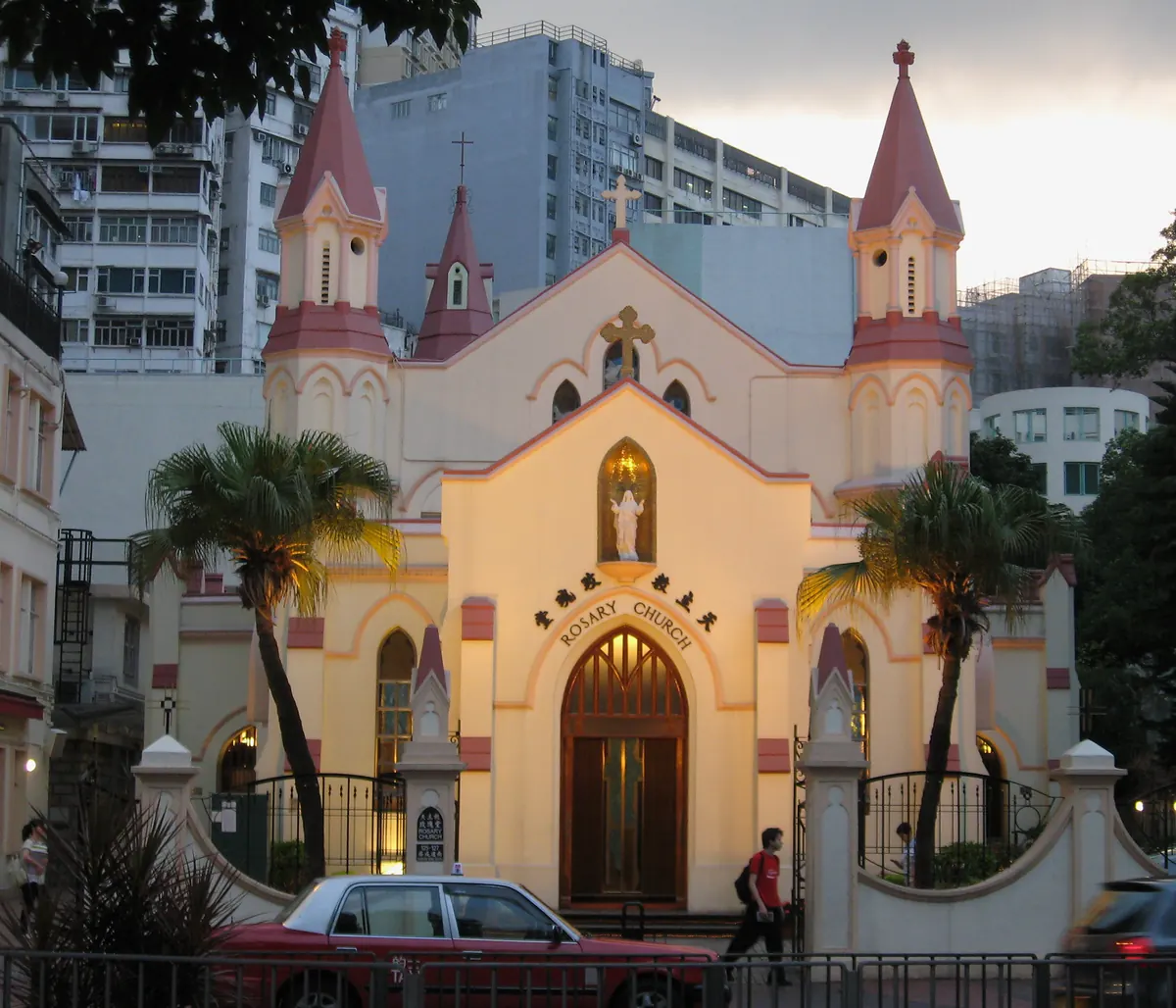 The cream-and-rose Gothic façade of Rosary Church on Chatham Road South in Tsim Sha Tsui, glowing in the evening light, with a statue of Our Lady in the niche above the door.