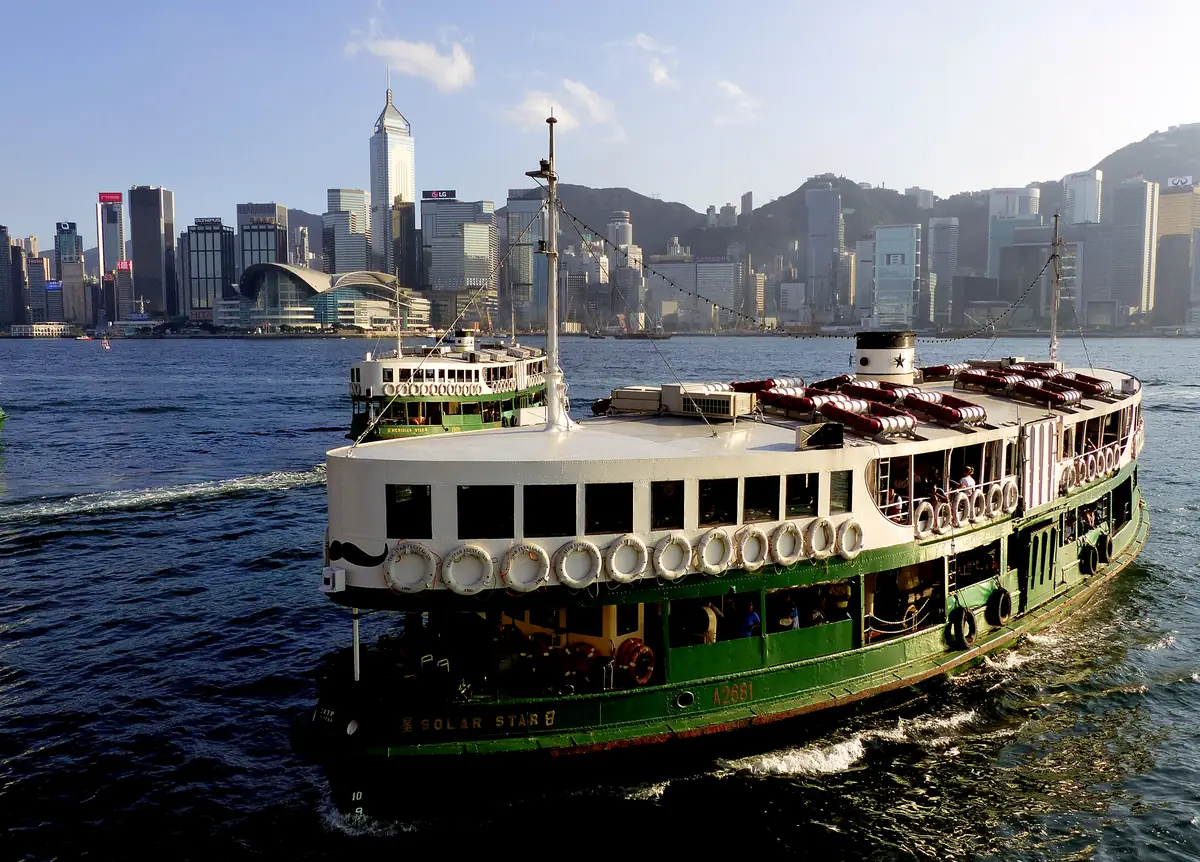 A green-and-white Star Ferry, the Solar Star, crossing Victoria Harbour in warm late-afternoon light with the Wan Chai skyline of Hong Kong Island behind it.