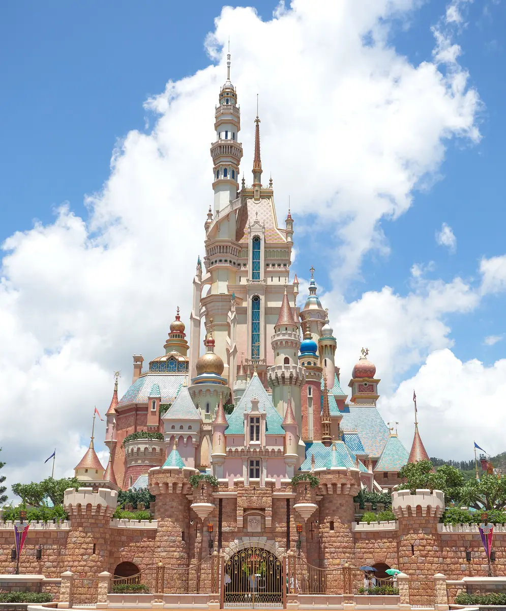 The Castle of Magical Dreams at Hong Kong Disneyland: pastel towers, turquoise roofs and golden domes rising against a blue sky with big white clouds.