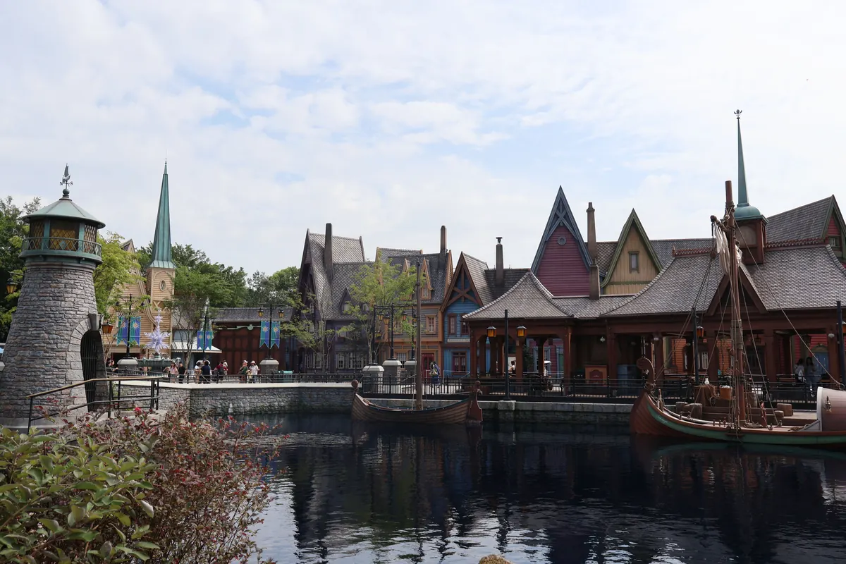 The fjord-side village of Arendelle in World of Frozen at Hong Kong Disneyland: a stone lighthouse, steep-roofed Nordic timber houses and a Viking-style ship moored on dark, still water.